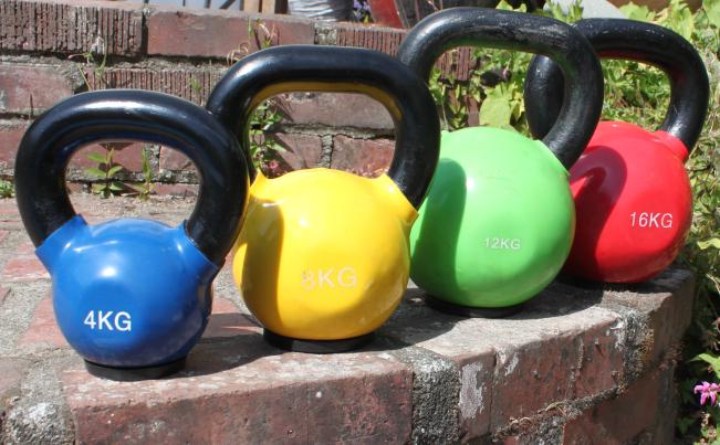 Four differently coloured kettle bells on a wall